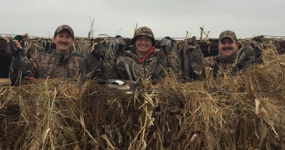 three waterfowl hunters holding up their ducks and geese